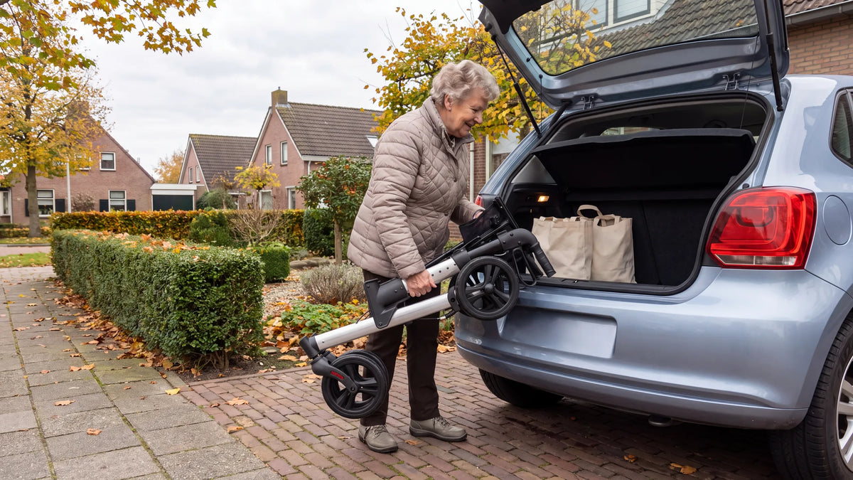 Ingeklapte Parvum Riva in grijs; een vrouw tilt hem op haar oprit in de kofferbak van haar auto.