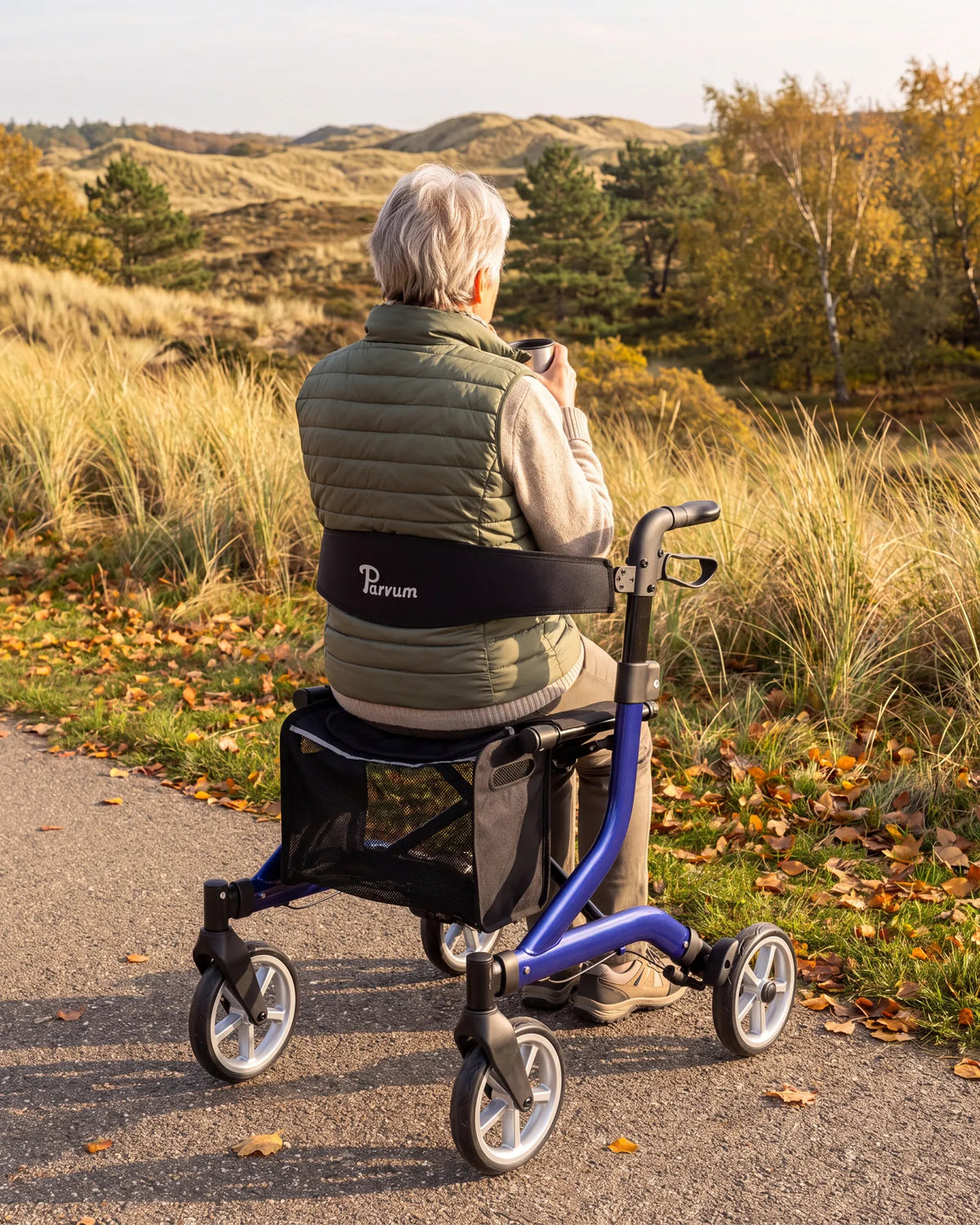 Parvum SuperLight Plus in blauw langs een pad; een vrouw zit op de rollator met een kop thee in haar handen.