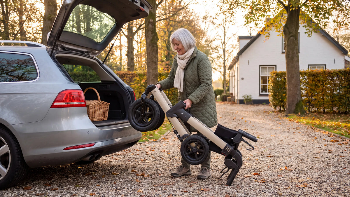 Ingeklapte Parvum Luxo Air in champagne; een vrouw tilt hem op een grindoprit in de kofferbak van haar auto.