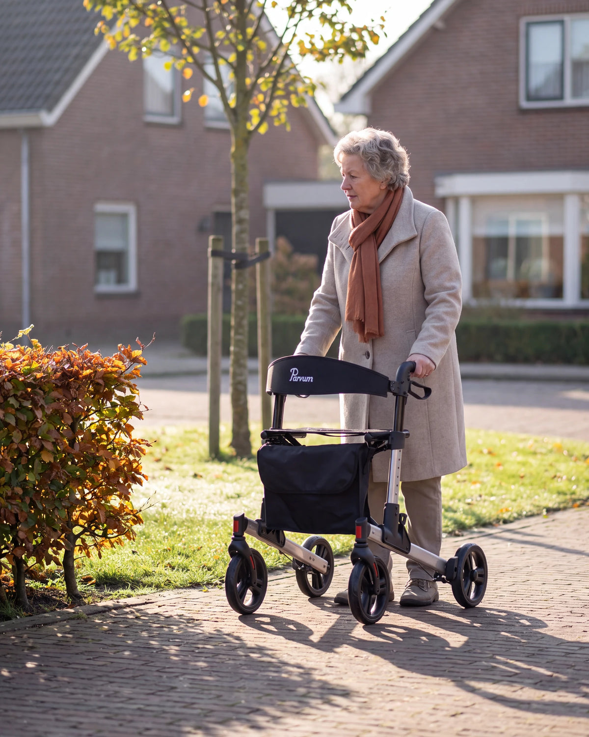 Parvum Riva in grijs op de stoep langs een beukenhaag; een vrouw in een wollen jas staat even stil.