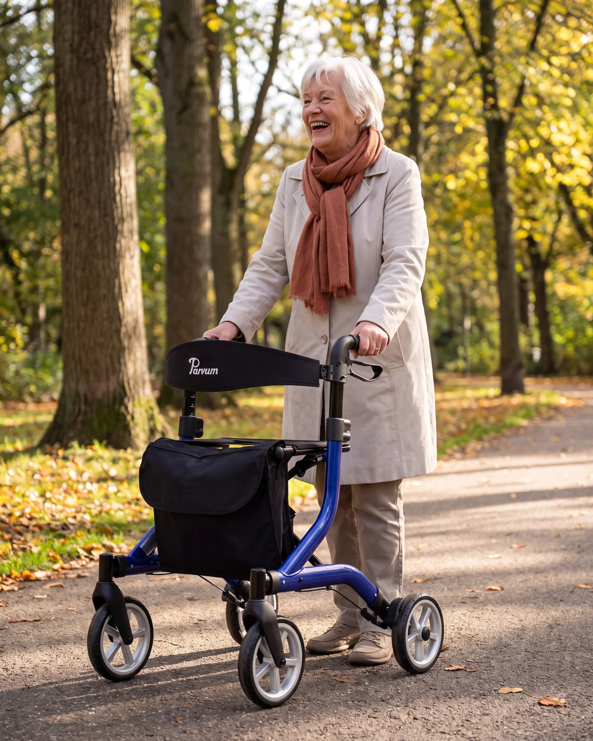 Parvum SuperLight in blauw onder hoge bomen in een park; een vrouw met wit haar lacht, haar handen op de handvatten.